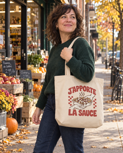 Sac écru J’apporte la sauce porté à l’épaule, motif rétro rouge sur le devant.