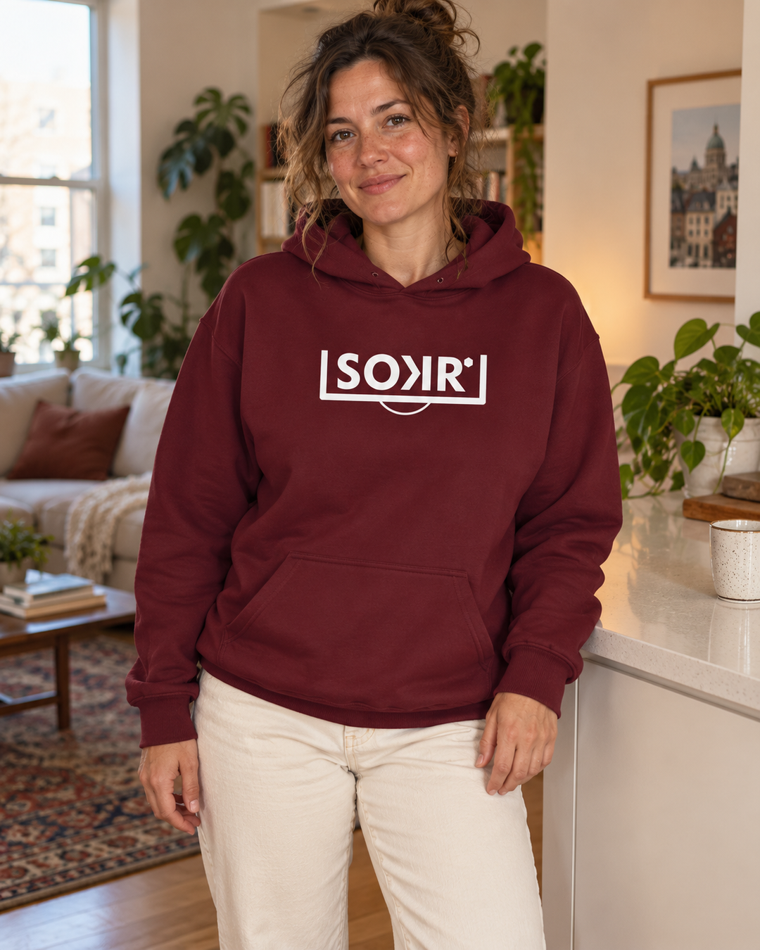 Hoodie SOKR bordeaux porté avec un pantalon écru dans un intérieur chaleureux.