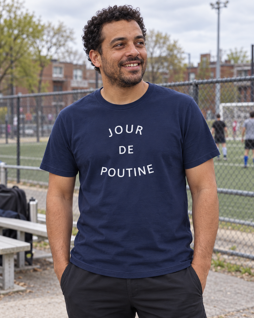 Homme portant le t-shirt bleu marine JOUR DE POUTINE au bord d’un terrain de soccer.