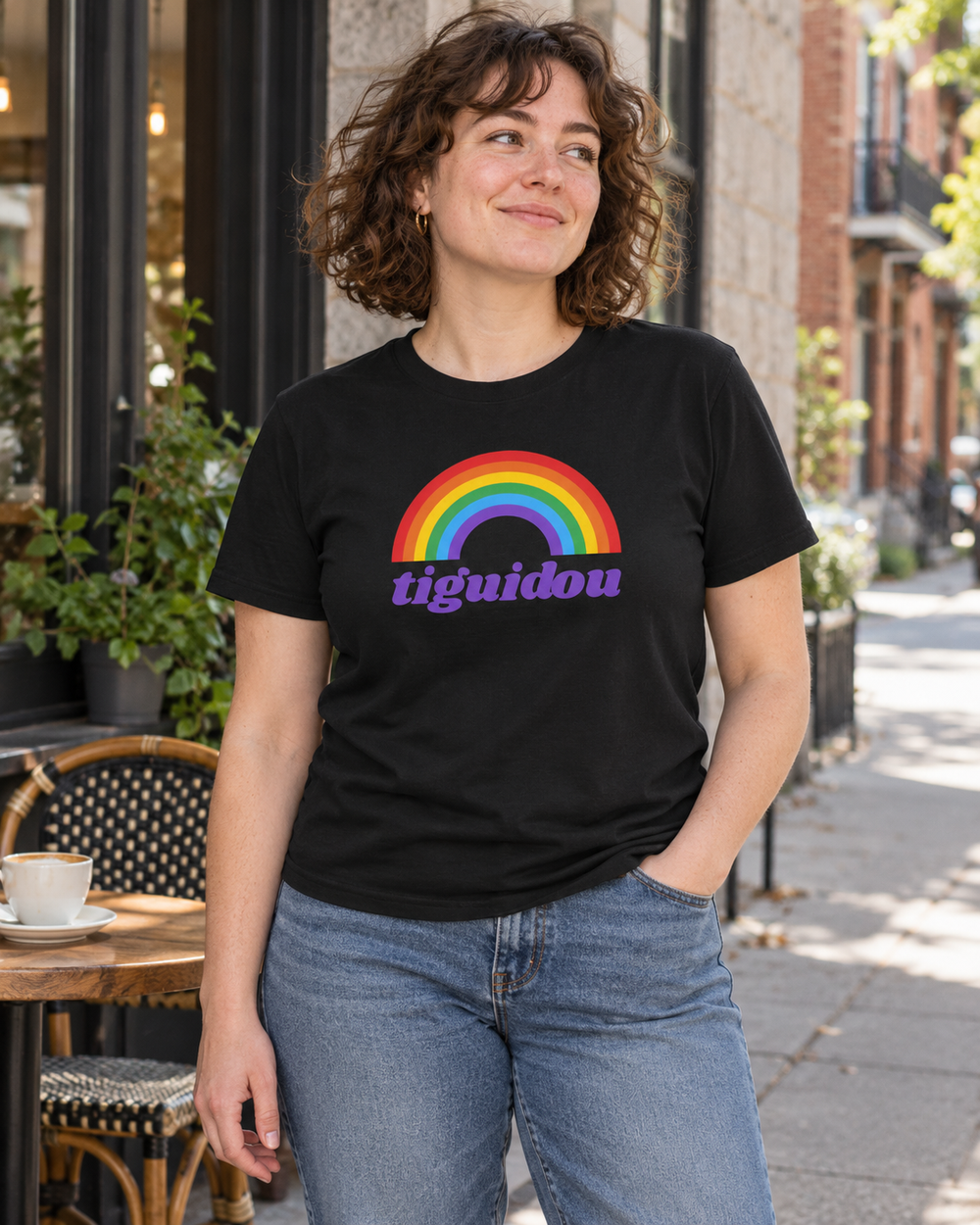 Femme portant le t-shirt noir TIGUIDOU à motif arc-en-ciel en terrasse.