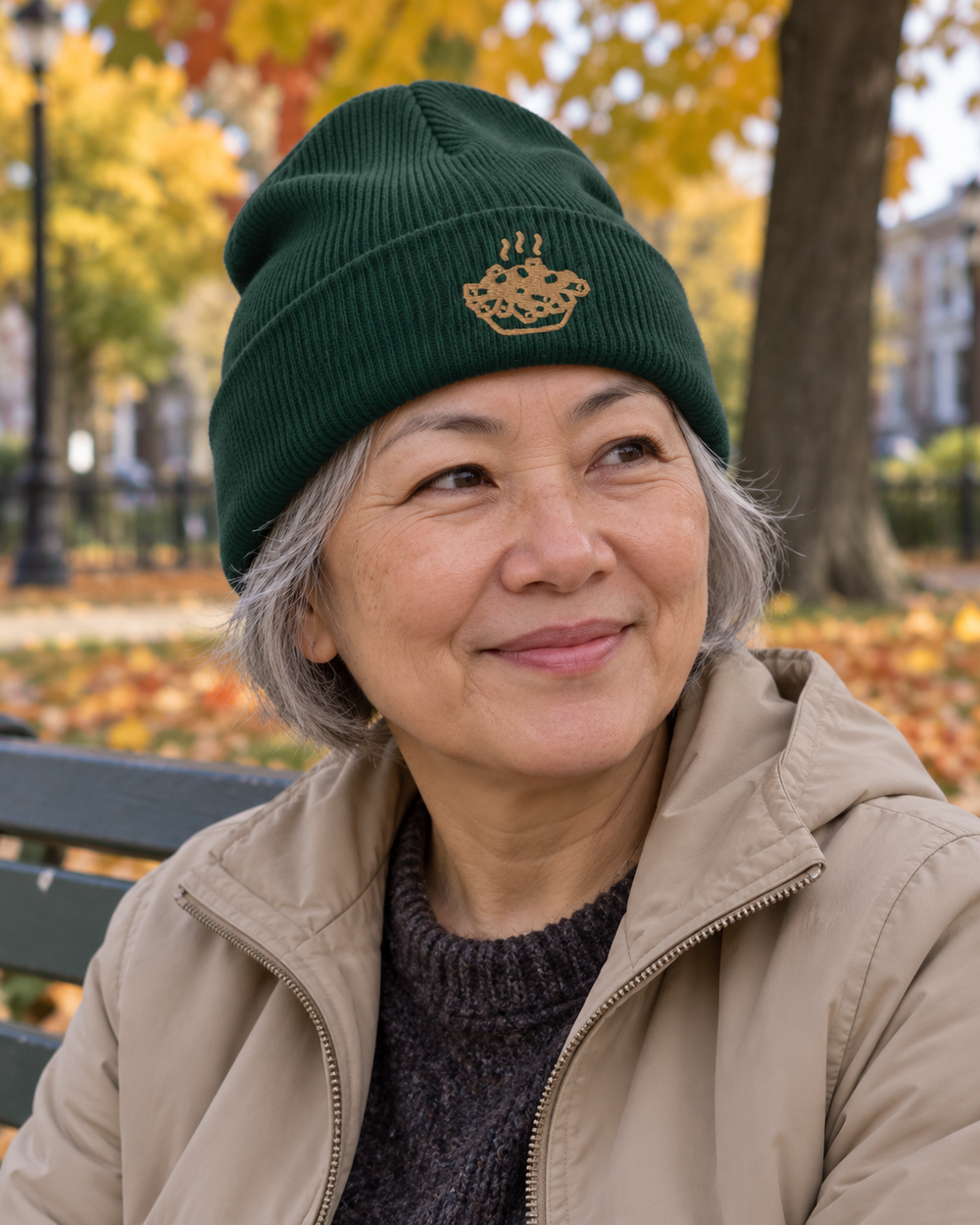Femme portant la tuque POUTINE vert épinette, broderie dorée, dans un parc.